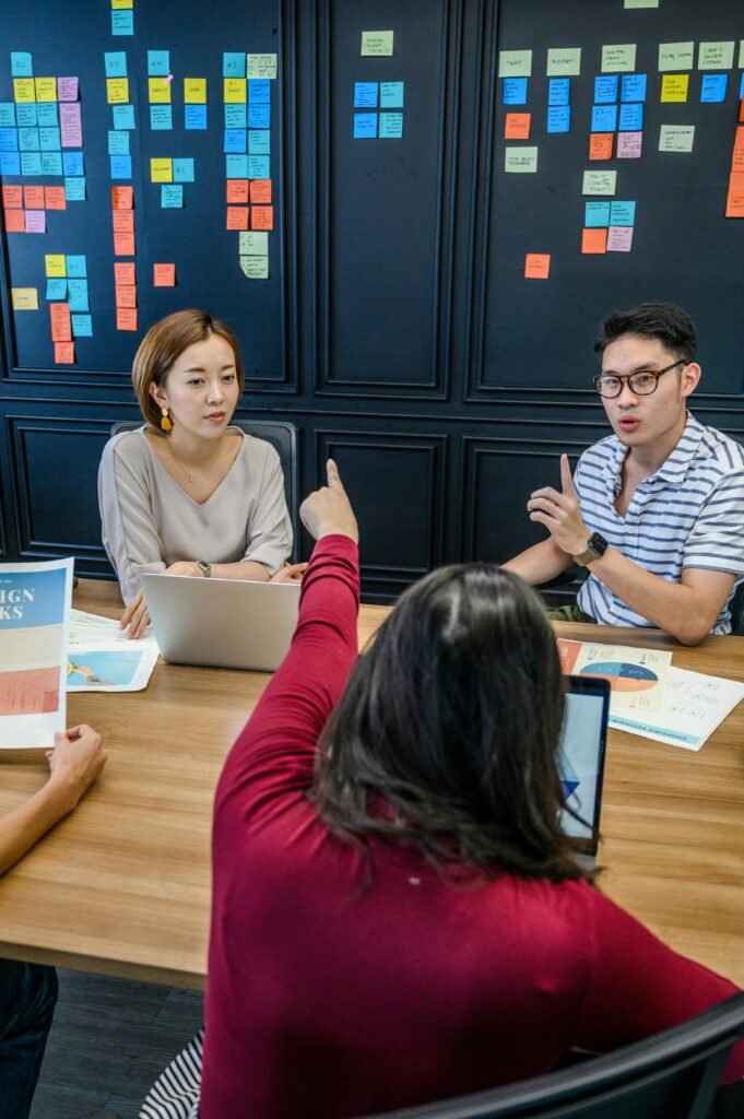 A team engaged in a collaborative meeting with laptops and colorful sticky notes on a wall.